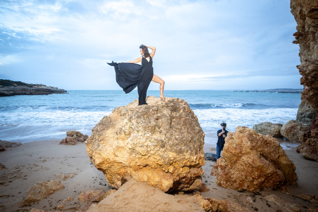 Frau im wehenden Kleid auf einem Felsen am Meer, Markus fotografiert