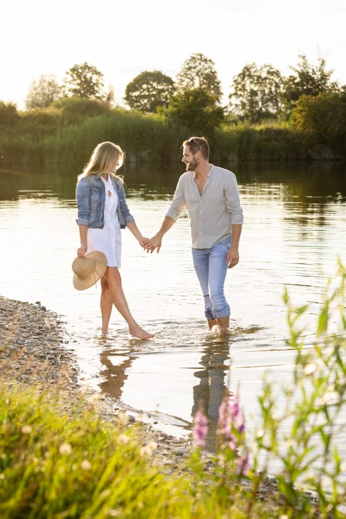 Paar geht Hand in Hand durch flaches Wasser am See
